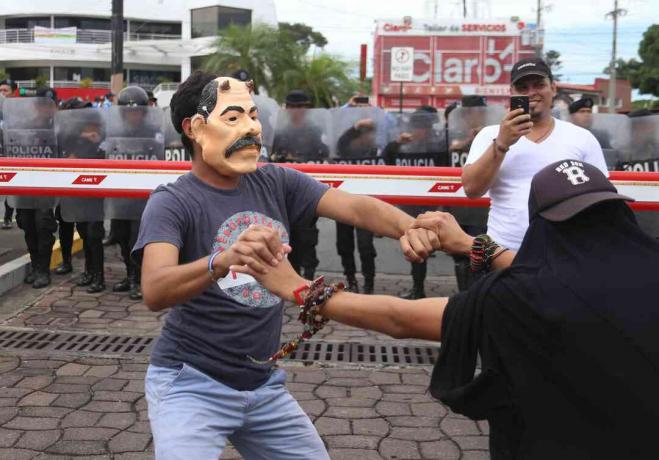 Een demonstrant draagt ​​een masker dat Daniel Ortega bespot
