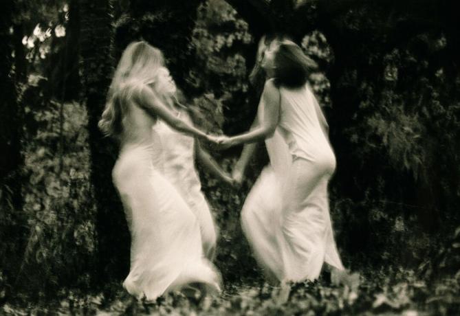 Vier jonge vrouwen dansen in het bos, hand in hand (B&W, wazig beweging)