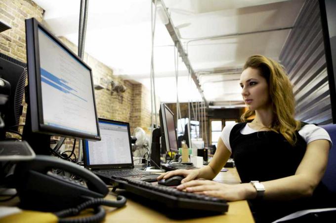 Een vrouw zit aan een bureau met behulp van een laptop met extern toetsenbord en monitor.