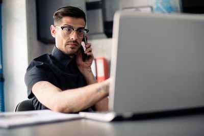 Man in bril op telefoon met behulp van laptopcomputer