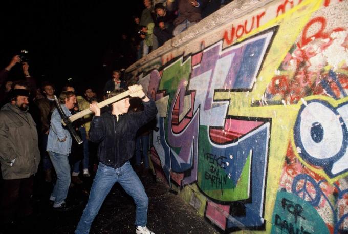 Een man valt de Berlijnse muur aan met een houweel in de nacht van 9 november 1989