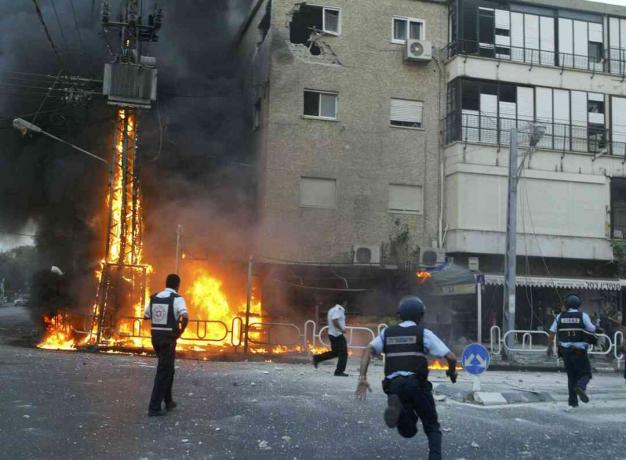 Israëlische politieagenten haasten zich naar de plaats van een brandende hoogspanningsmast en beschadigde gebouwen, kort nadat een salvo Hezbollah-raketten op 13 juli 2006 in de noordelijke stad Nahariya, Israël, troffen.