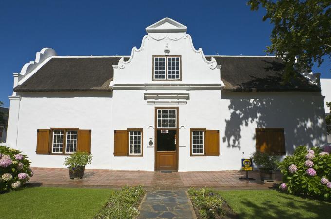 wit huis met grote muur die uitsteekt boven de rontdeur en aan de geveluiteinden