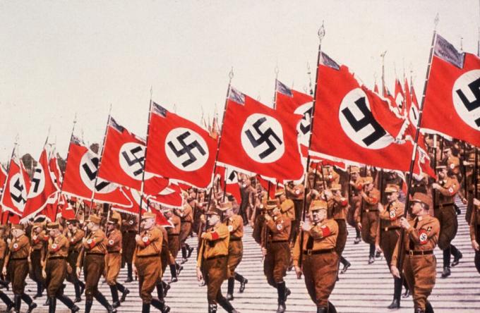 Nazi's marcheren in formatie met vlaggen tijdens een rally.