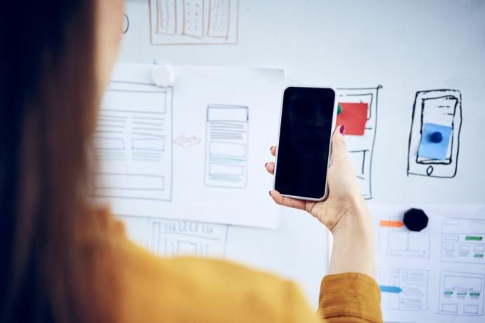 Vrouw met smartphone en kijken naar ideeën voor webdesign op whiteboard