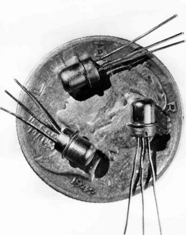 Foto uit 1956 van drie miniatuur M-1 transistors gezien op de voorkant van een dubbeltje