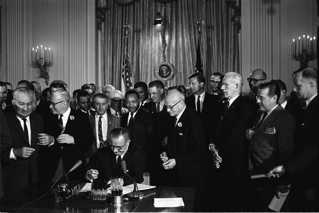 Voorzitter Lyndon B. Johnson ondertekent de Civil Rights Act van 1964 terwijl Martin Luther King, Jr. en anderen toekijken.