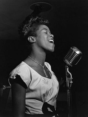 Sarah Vaughan zingt in een microfoon, zwart-wit foto.